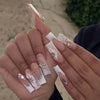 A close-up of a hand displaying elegant white and silver glitter nail art designs on fingernails.
