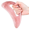 Una mano sostiene una herramienta gua sha de resina rosa con patrones marmolados para masaje facial y corporal.