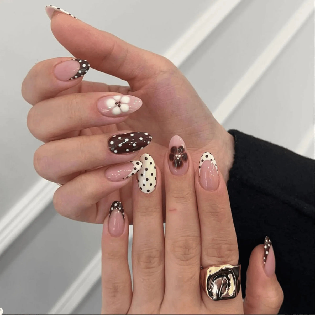 A hand displays various red and pink striped press-on nails on fingers.