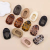 A collection of oval flat hair clips in various colors including black, brown, beige, and white.