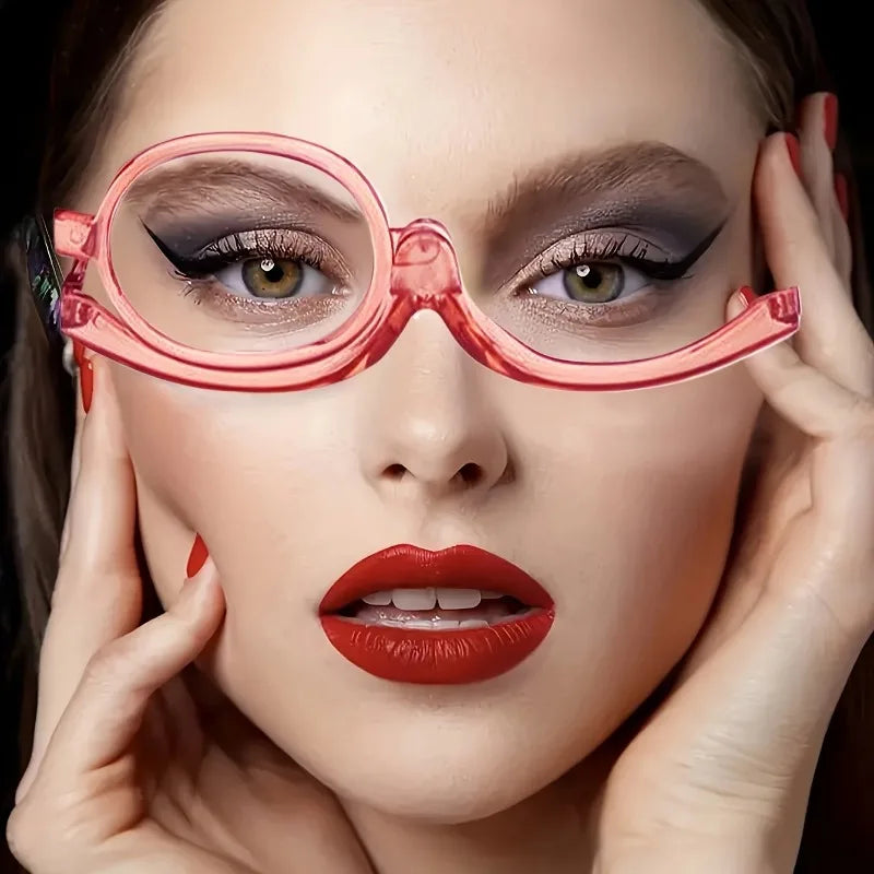 A woman wearing pink magnifying reading glasses with dramatic eye makeup and red lipstick.