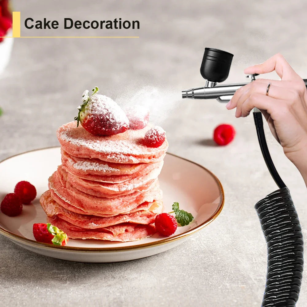 A hand uses a portable airbrush kit to decorate a stack of strawberry pancakes with powdered sugar and fresh berries.