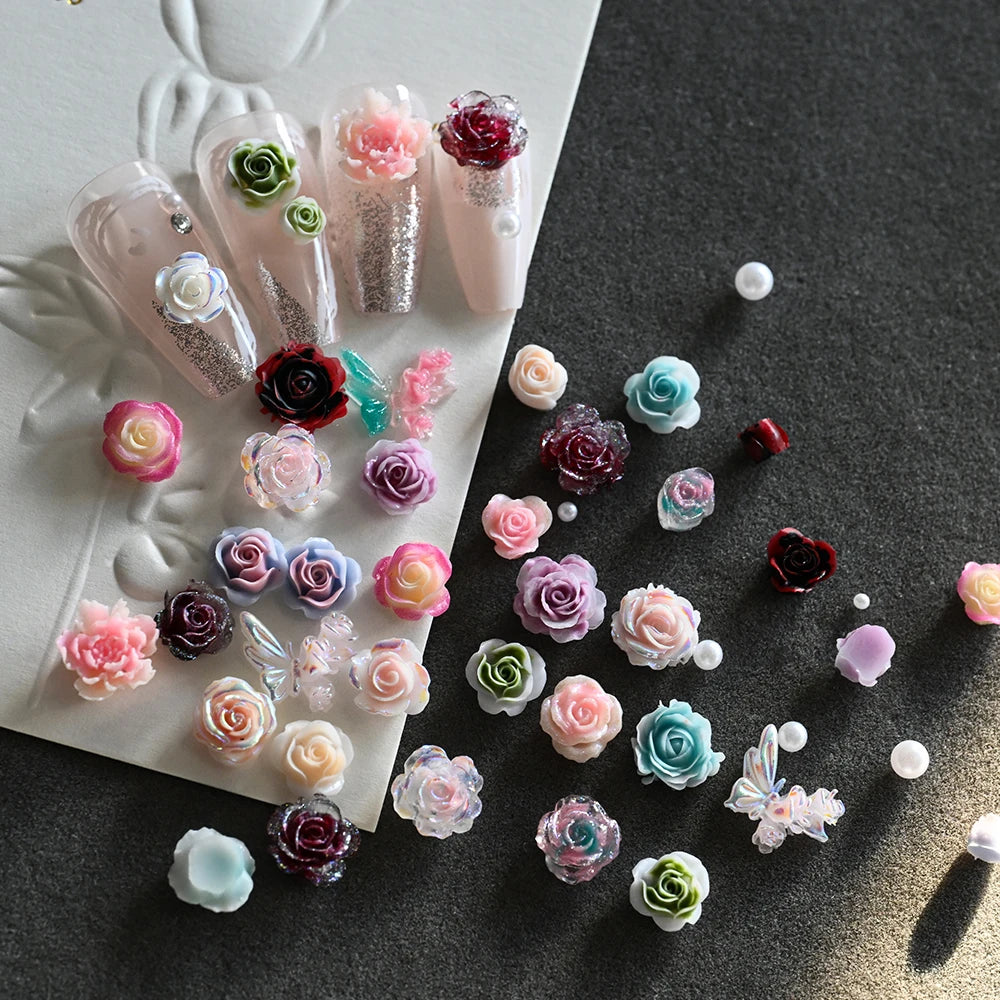 A collection of 3D floral butterfly pearl nail art charms in various shades of pink, purple, and green arranged on a dark sur
