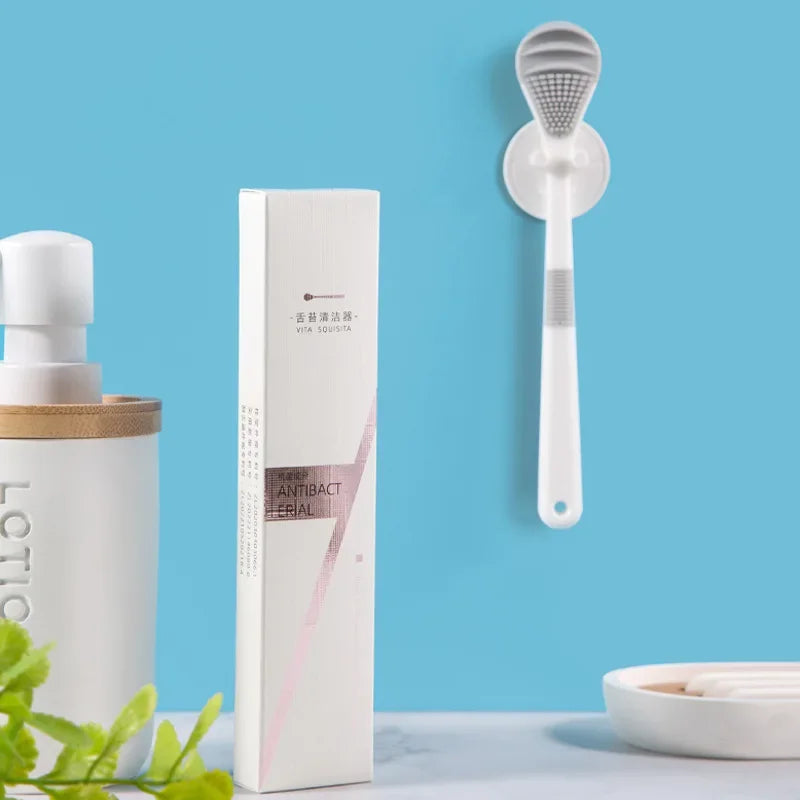 A white reusable tongue cleaner brush hanging on a blue wall next to a white bottle.