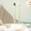 Une paire de brosses à dents micro-nano vert clair posées sur une serviette beige douce avec de la peluche blanche.