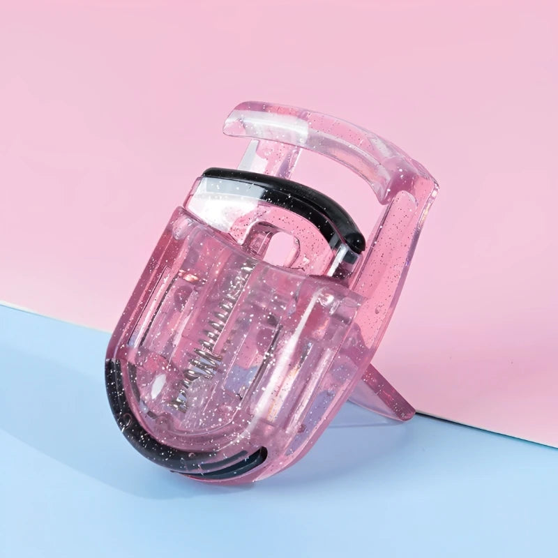 A pink portable mini eyelash curler set with a black handle and clear casing is shown on a light blue surface.