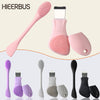Colección de herramientas de masaje facial de silicona rosa y morada, incluyendo un cepillo de paletas, rodillos faciales y d