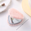 A heart-shaped foldable travel makeup mirror covered in pink faux fur resting on a white surface.