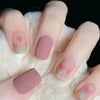 A hand displays a set of press-on acrylic nails with a soft pink and green floral design on a white fluffy background.