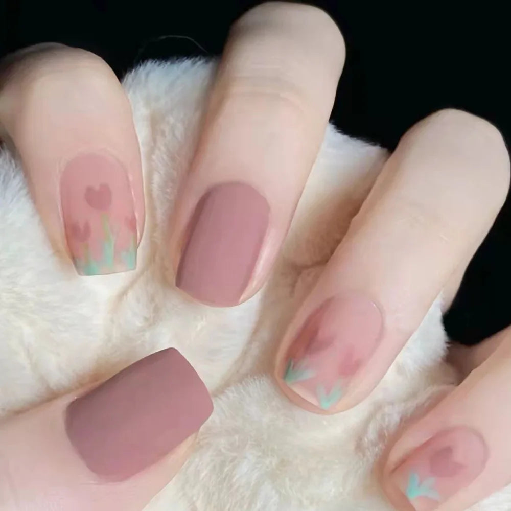 A hand displays a set of press-on acrylic nails with a soft pink and green floral design on a white fluffy background.
