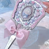 A pink and silver decorative makeup mirror with a satin ribbon bow being held by a hand.