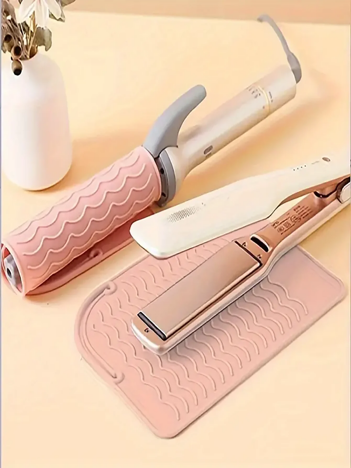 A pink silicone heat resistant mat is shown with a hair styling tool and its cleaning brush on a light background.