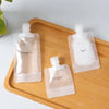 A set of three clear plastic squeeze bottles for refillable travel toiletries placed on a wooden tray.