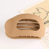 A beige oval flat hair clip is shown resting on a piece of paper with a line drawing.