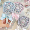 A hand holding a set of decorative pearl-themed mirrors with pink and blue accents for makeup and beauty.