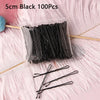 A clear plastic bag containing 100 black 5cm metal U-shaped hair pins is displayed on a pink fluffy surface.