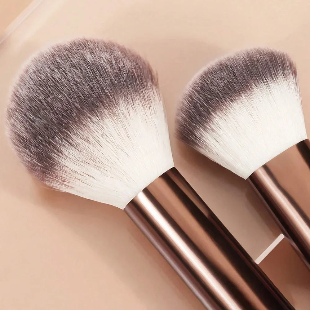 Un par de brochas de maquillaje profesionales con cerdas plateadas y blancas sobre un fondo claro.