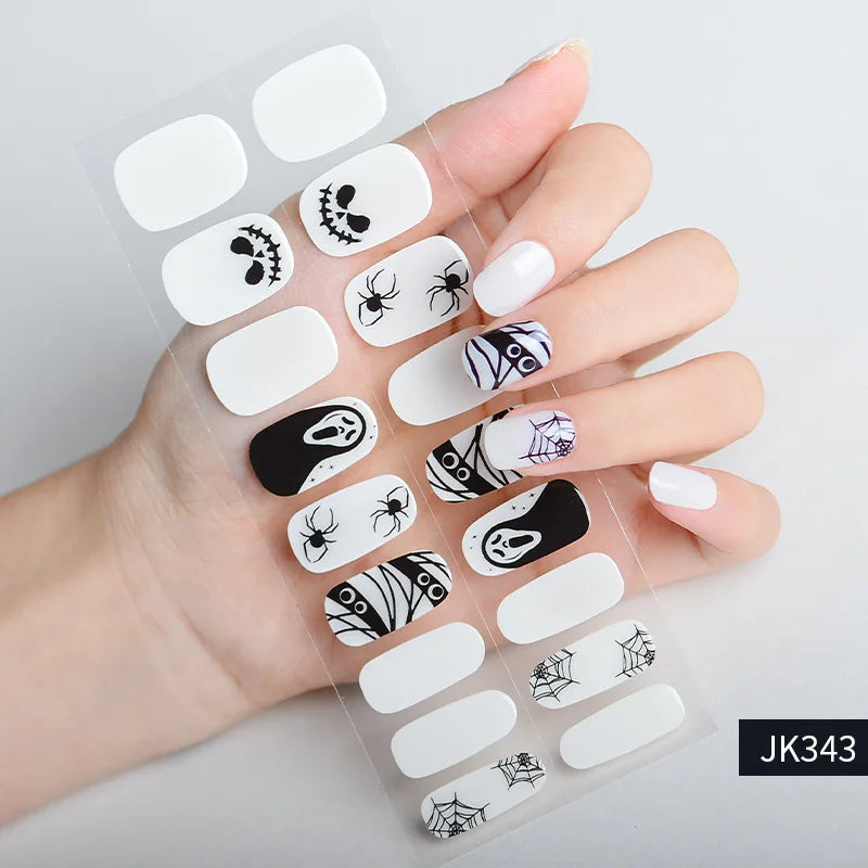 A hand holds a sheet of Halloween UV gel nail stickers featuring black and white spider and bat designs.