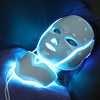 A person is using a glowing blue LED facial mask for skin rejuvenation on their face.
