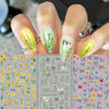A hand displays various floral and butterfly nail stickers in yellow, green, and pink shades for DIY decoration.