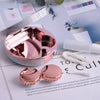 A pink round contact lens storage box with a marble pattern is shown next to some white cosmetic items.