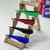 A wooden rack displays five folding shaving razors in various colors including green, red, black, and blue.