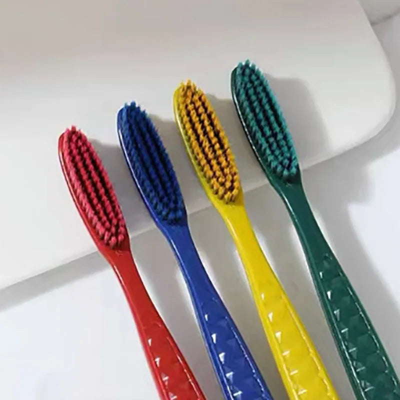 Un set de cinq brosses à dents colorées et douces disposées en diagonale sur une surface blanche.
