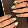 Close-up of fingers displaying reusable fake nails with a gold and black polka dot pattern on almond shaped tips.