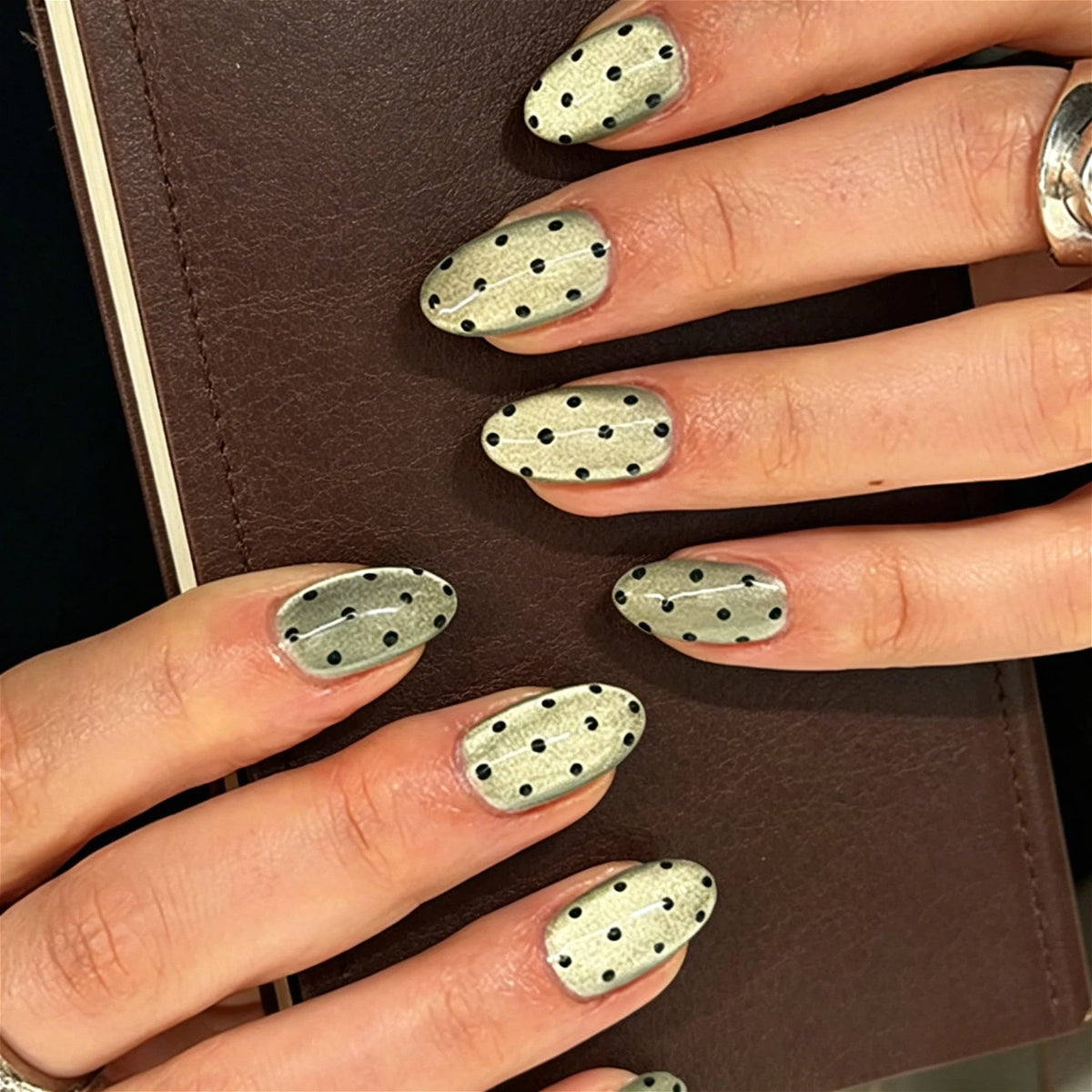 Close-up of fingers displaying reusable fake nails with a gold and black polka dot pattern on almond shaped tips.