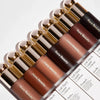 A collection of Rare Beauty liquid bronzer contour foundation sticks arranged in a diagonal line.