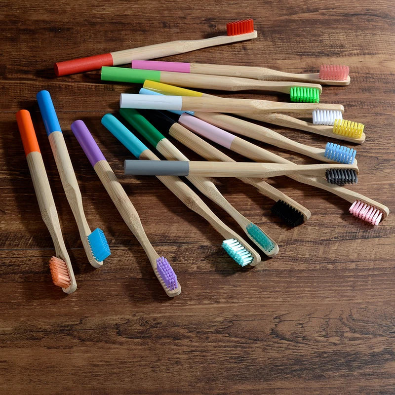 A collection of ten eco-friendly bamboo toothbrushes in various colors and sizes laid out on a wooden surface.