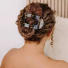 A woman's hair is styled in an updo with oval flat leopard print clips visible on the back of her head.