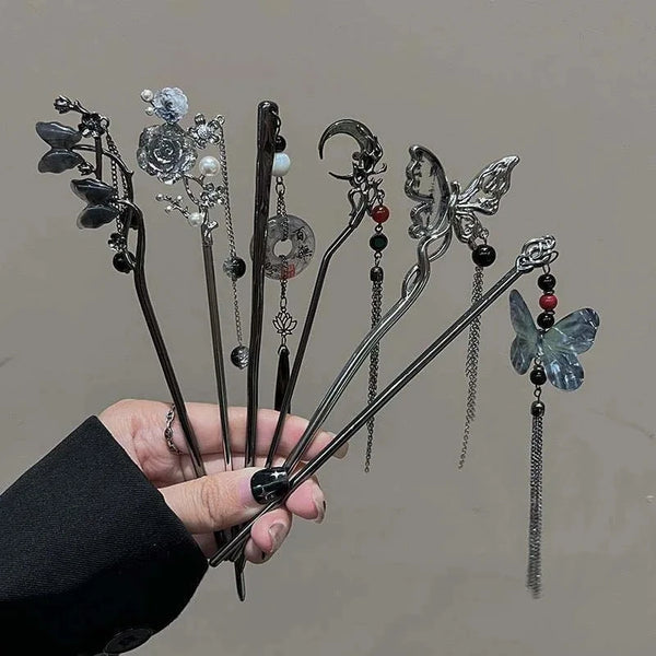Eine Hand hält mehrere Vintage-Silber-Schmetterlings-Haarstäbchen mit verschiedenen Anhängern und Perlen.