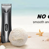 A black electric body hair trimmer stands next to natural sea elements like shells and sand.