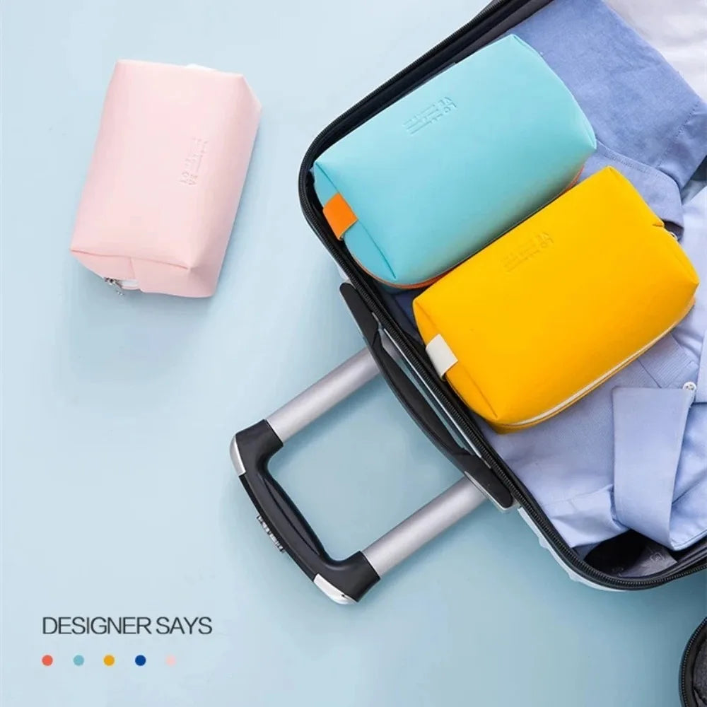 A black makeup bag is open, displaying three colored cosmetic pouches: pink, light blue, and yellow.