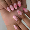 Gros plan de mains montrant des kits de ongles fleurs à noisette pressées dans diverses nuances de rose et de blanc.