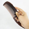 Eine Hand hält eine dunkelbraune, hohle Anti-Haarausfall-Massagebürste mit feinen Zähnen.