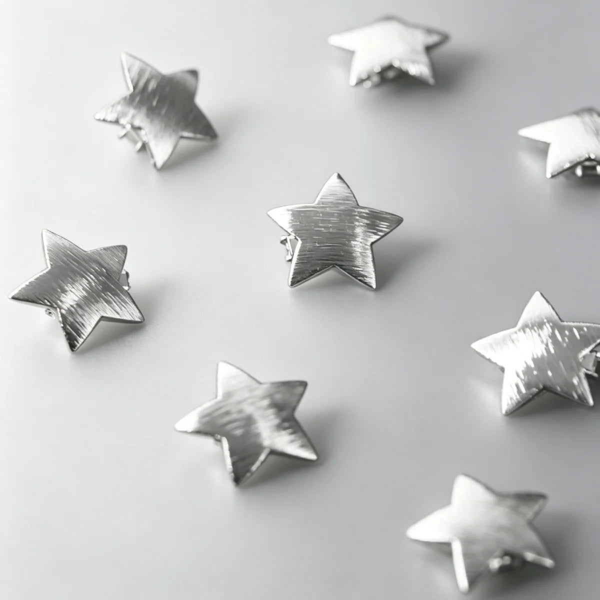 A collection of ten star-shaped hairpins with silver and gold finishes scattered on a light gray background.