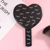 Miroir à cils en forme de cœur noir à main avec poignée sur fond rose.