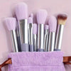 A collection of thirteen professional makeup brushes in various shades of purple and silver resting on a lavender towel.
