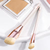 A pair of light pink makeup brushes with gold accents are displayed next to an open makeup palette.