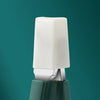A white ergonomic beveled nail clipper is shown resting on a green surface against a teal background.