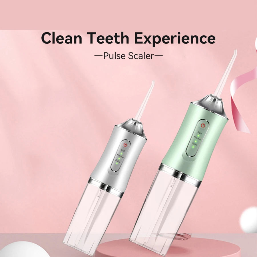 A close-up of a handheld pulse scaler dental flosser with a light green and silver body resting on a pink surface.