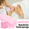 A woman is using pink facial sponges on another person's face in a spa-like setting with packaged sponges visible.