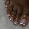A close-up of a hand with short square French press-on nails featuring glitter and purple accents