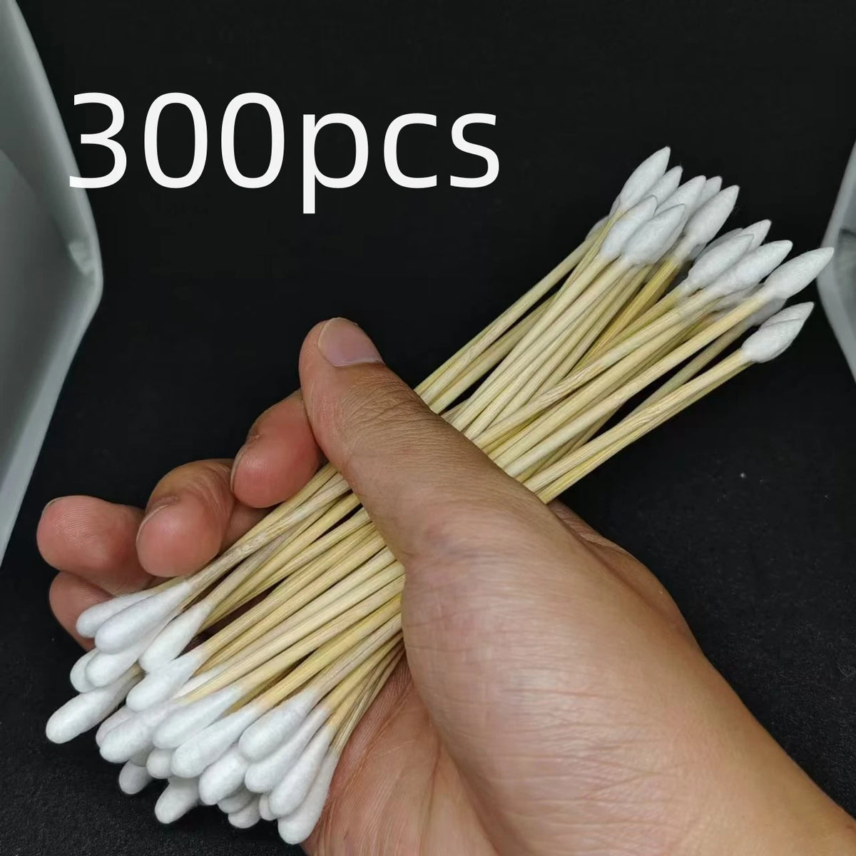 A hand holds a bundle of 300 precision wooden cotton swabs with white tips.
