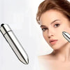 A woman is using a silver mini facial eye massager on her face.