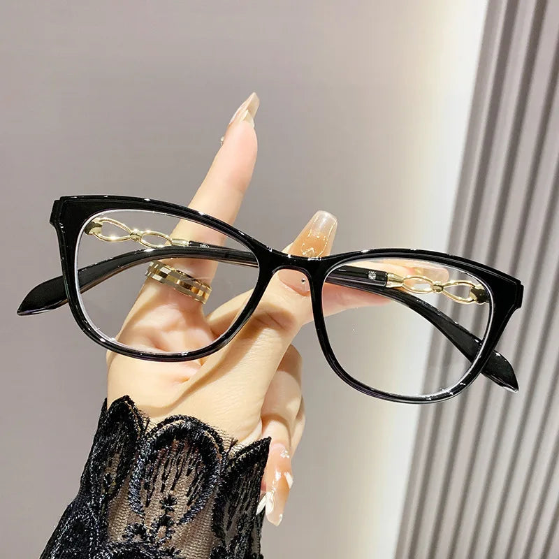 Lentilles de lecture à œil de chat noires avec accents dorés, tenues par une main portant des gants en dentelle.