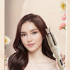 A woman models a wavy hairstyle while holding an automatic ceramic hair curler stick.