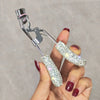 A hand holds a professional eyelash curler set with silver metal tools and glittery silicone curlers.